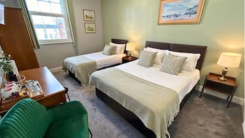 A hotel room with two beds, a desk, a chair, and a window.