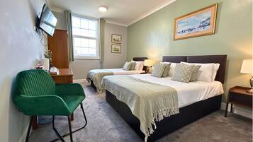 A hotel room with two beds, a green chair, a flat-screen TV, and a painting on the wall.