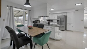 A modern kitchen with white cabinets, a stainless steel refrigerator, and a dining area with a wooden table and chairs. - Spacious, Modern, Healing Home in Columbus (Columbus)