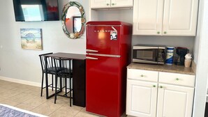 A compact kitchen with a red refrigerator, white cabinets, a microwave, and a small dining area with two chairs. - Beachgate Condo Suites And Hotel 435 1 Bedroom Condo (Port Aransas)