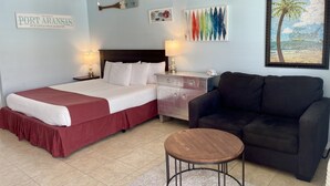A hotel room with a bed, a nightstand, a lamp, a couch, a coffee table, and a ceiling fan. - Beachgate Condo Suites And Hotel 435 1 Bedroom Condo (Port Aransas)