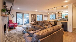 A modern living room with a large sectional sofa, a red armchair, and a fireplace. There is a kitchen area with a bar and pendant lighting. - 5 Wickiup 3 Bedroom Home by RedAwning (Bend)