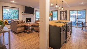 A modern living room with a fireplace, leather sofa, and a dining area with a kitchen island. - 5 Wickiup 3 Bedroom Home by RedAwning (Bend)