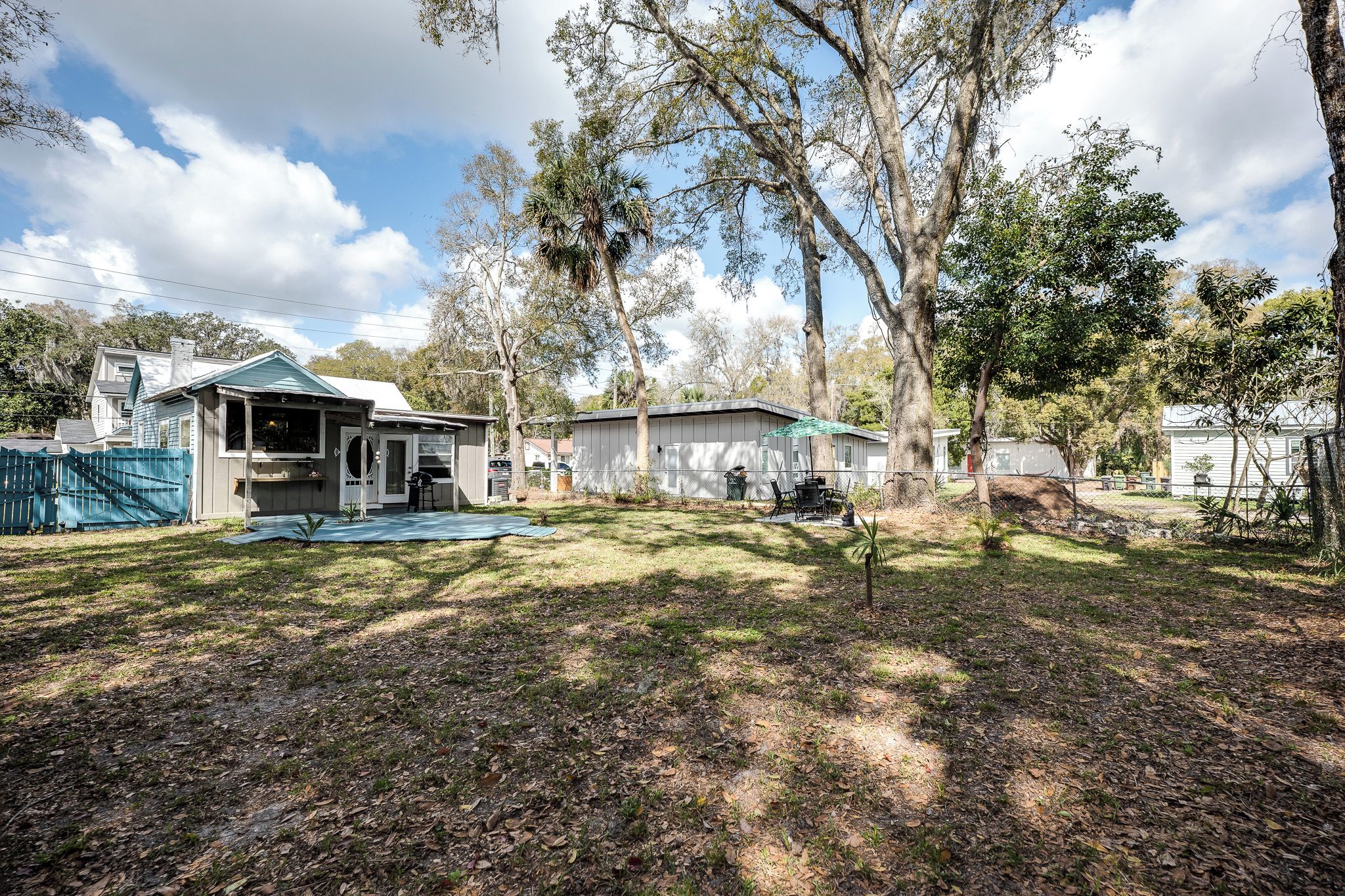 A residential property with a covered patio, a fenced yard, and mature trees.