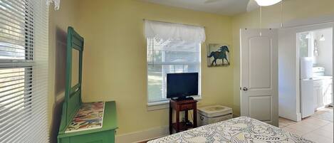 A bedroom with a bed, a television, a green dresser, a window with blinds, and a ceiling fan.