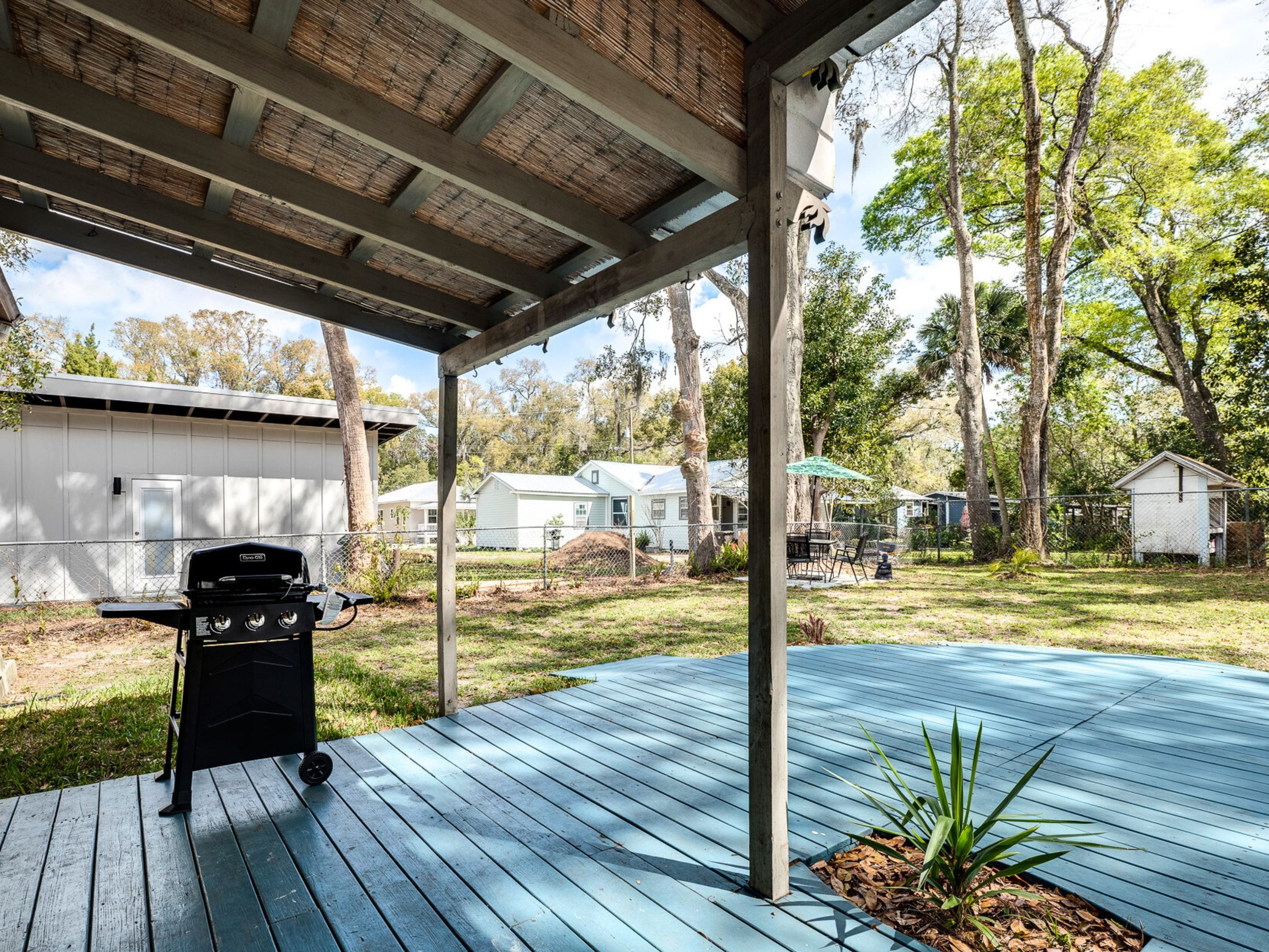 A covered outdoor deck with a grill, surrounded by a fenced yard with multiple mobile homes.