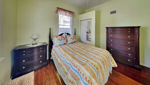 A bedroom with a bed, dresser, nightstand, and a window with blinds. - Cozy Casita by Distinctive Beach Rentals (St. Augustine)