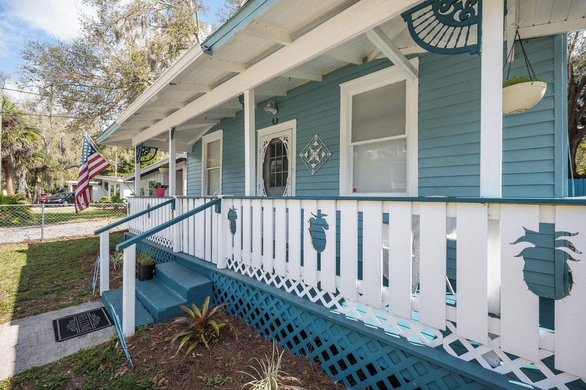 A porch with a blue railing, a white fence, and a small American flag.