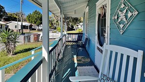A porch with a blue and white color scheme, a white chair with a patterned cushion, and a decorative wall piece. - Cozy Casita by Distinctive Beach Rentals (St. Augustine)
