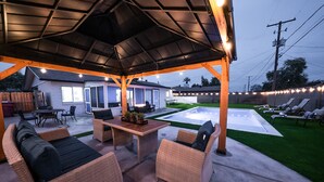 Una veranda coperta all'aperto con mobili in vimini, un tavolo con piano in vetro e una zona piscina.