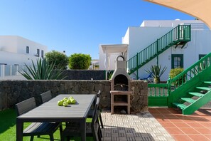En udendørs terrasse med en stenvæg, et bord med stole og en grøn trappe.