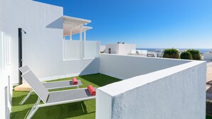 Une terrasse sur le toit avec des murs blancs, une petite pelouse et deux chaises longues.