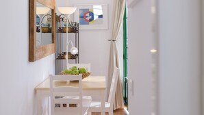 Un coin repas avec une table blanche, des chaises, un miroir à cadre en bois, une lampe et une œuvre d’art abstraite encadrée.