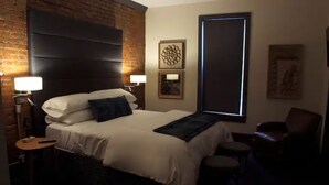 Une chambre d’hôtel avec un grand lit, un mur décoratif en briques, une tête de lit moderne, deux lampes de chevet, une petite table et une chaise.