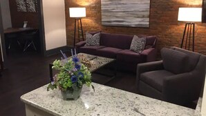 Un salon avec un mur en briques, un canapé violet, une table basse et deux lampadaires.