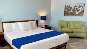 A neatly made bed with white and blue bedding, a bedside lamp, a clock, and a green sofa in a room with wooden flooring.