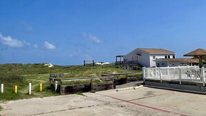 A coastal property with a wooden deck, a white fence, and a house with a brown roof.