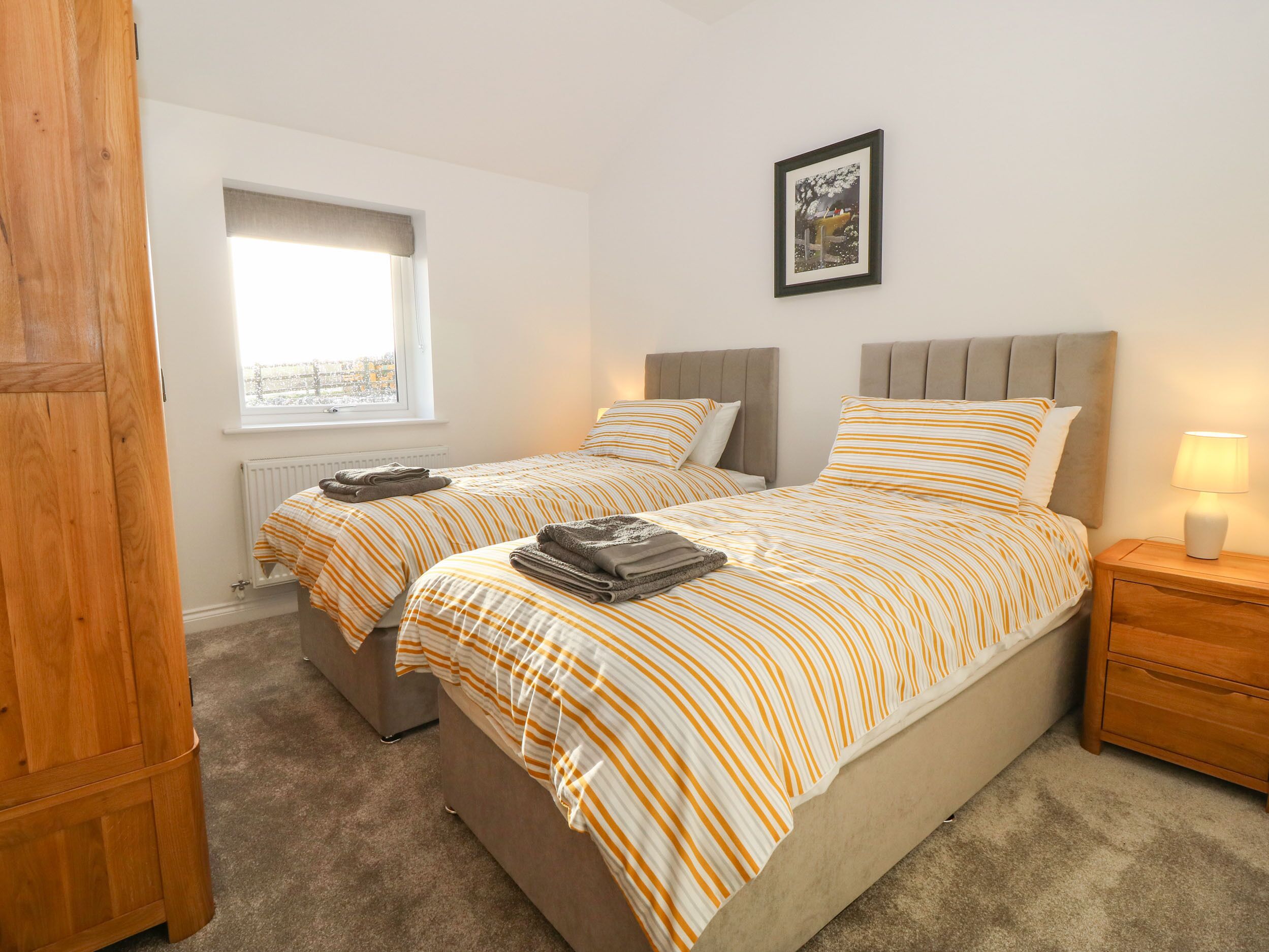 A bedroom with two beds, a window, a radiator, and a bedside table with a lamp.