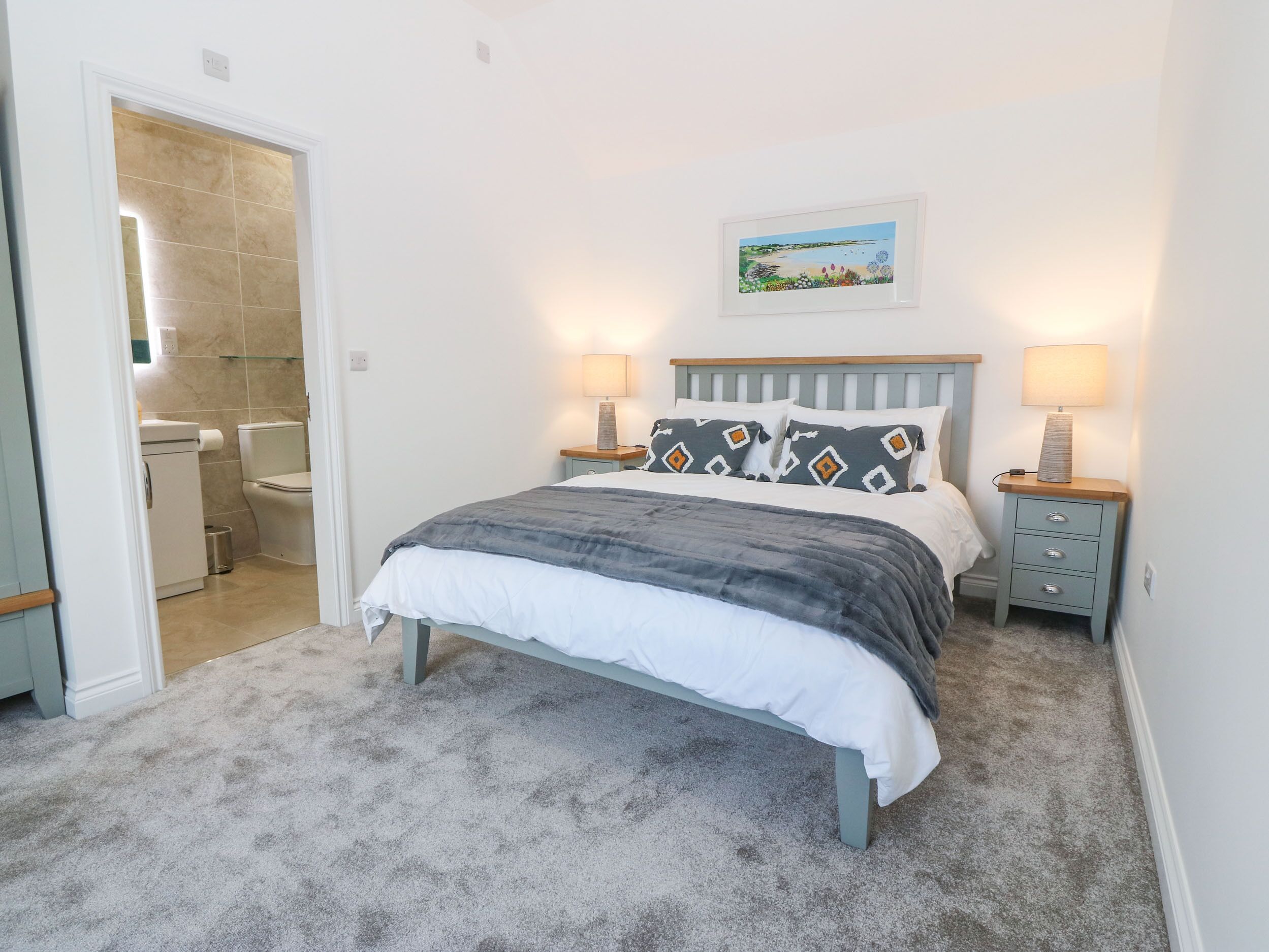 Une chambre à coucher avec un lit, deux tables de chevet, une commode, une lampe fixée au mur et un tableau au-dessus du lit.