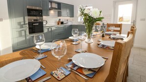 Eine moderne Küche mit grauen Schränken, Edelstahlgeräten und einer Essecke für sechs Personen mit Holzkästen und einer zentralen Blumenvase.