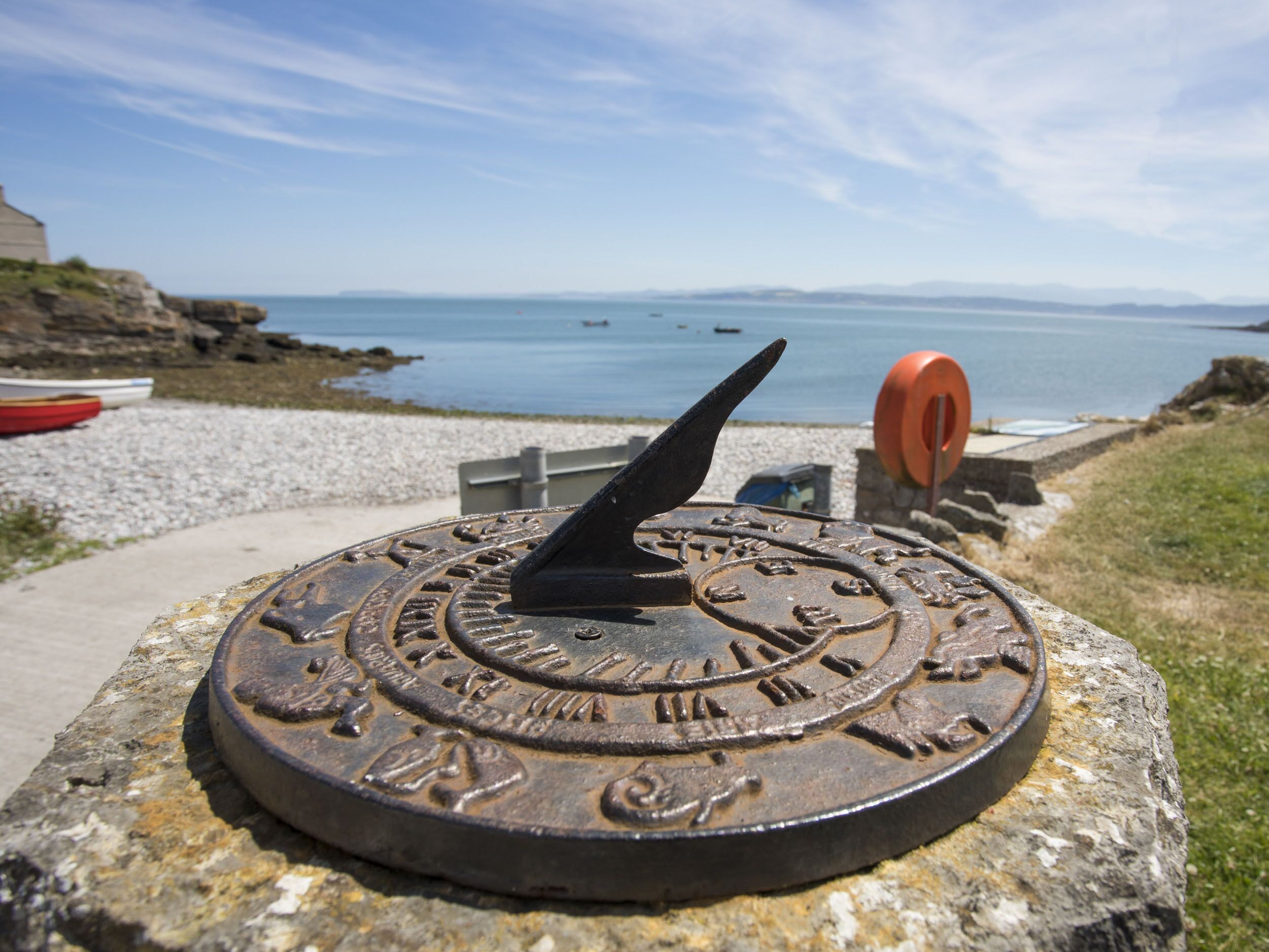 A weather station with a compass and a view of the sea and mountains in the background.