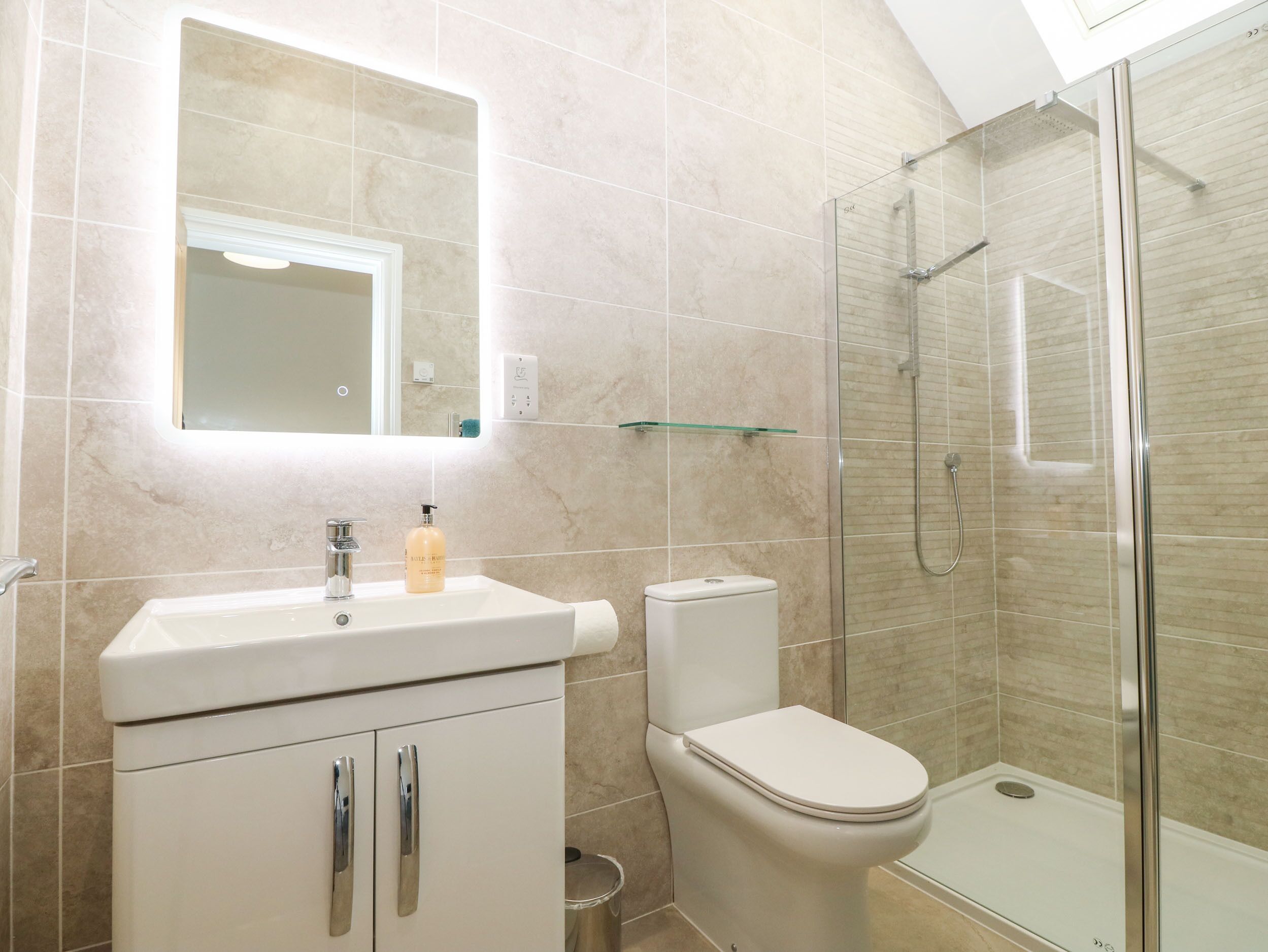 A modern bathroom with a glass shower enclosure, a white sink with a soap dispenser, and a toilet.