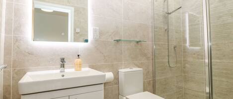 A modern bathroom with a glass shower enclosure, a white sink with a soap dispenser, and a toilet.