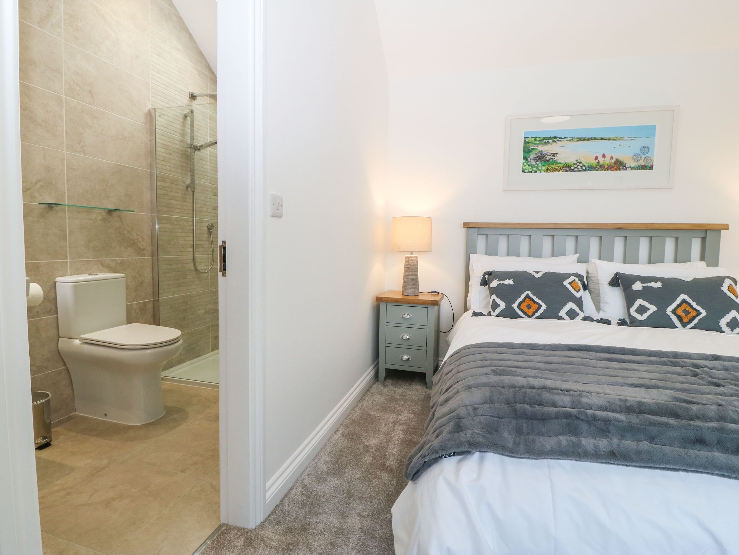 A bedroom with a bed, a nightstand, a lamp, a painting, and a shower area.