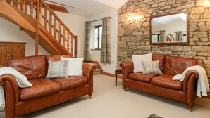 A living room with two brown leather sofas, a wooden staircase, a stone wall, and a large mirror. - Bullfinch Cottage (Leominster)