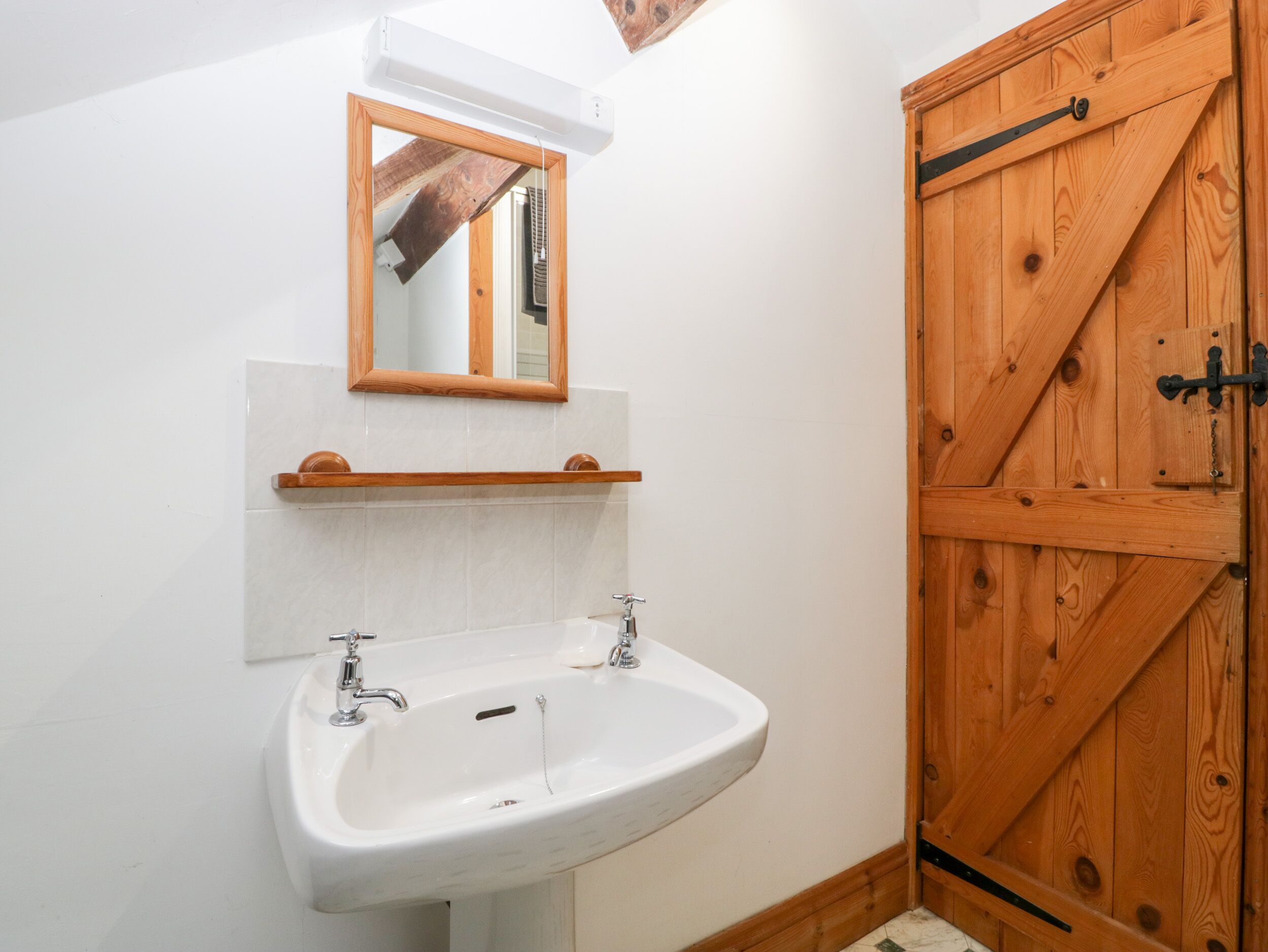 Un baño con un lavamanos blanco, una puerta de madera y un espejo sobre el lavamanos.