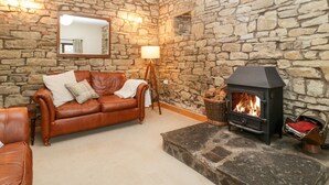 A cozy living room with a stone wall, a leather sofa, a fireplace, and a mirror. - Bullfinch Cottage (Leominster)