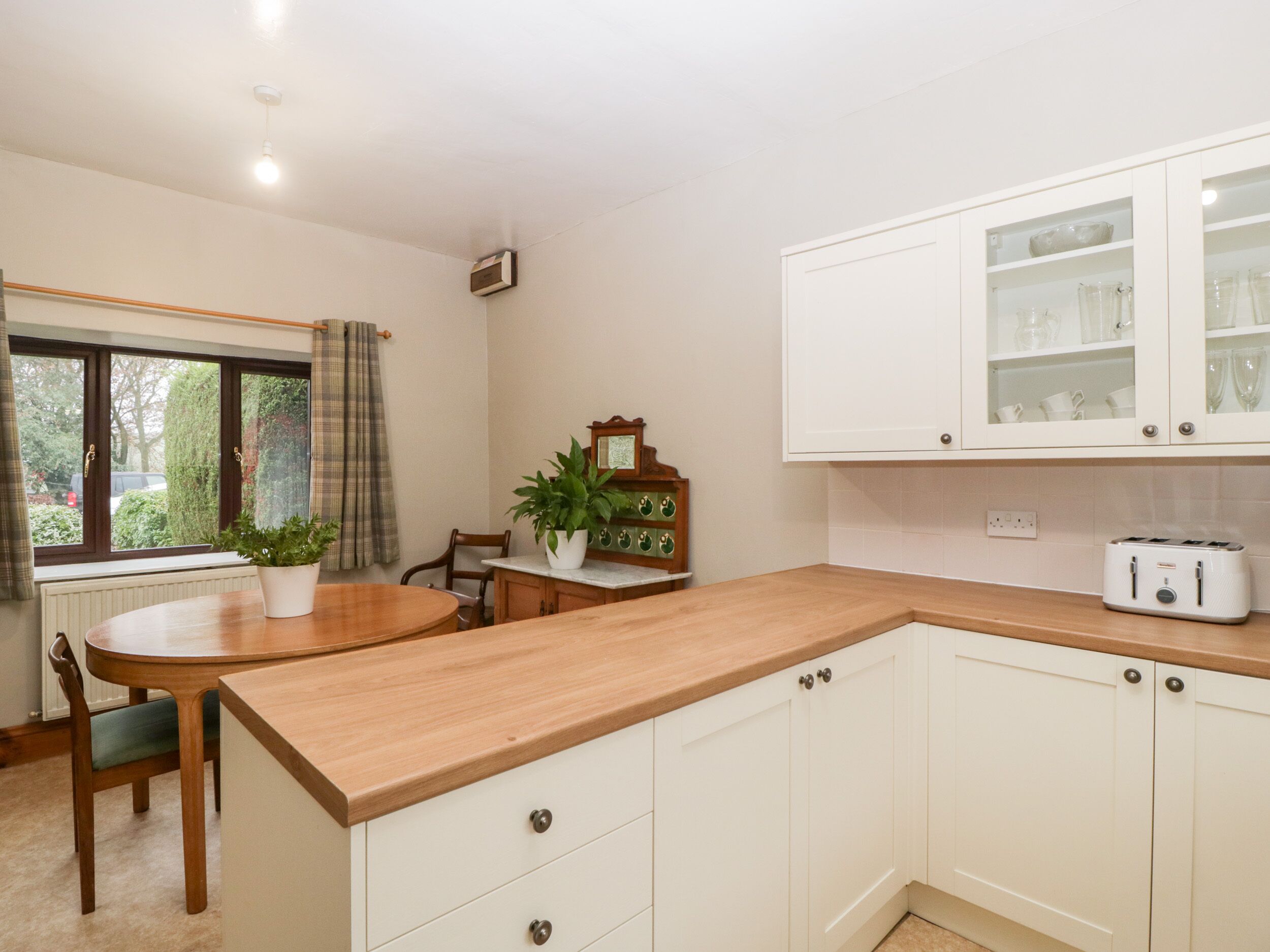 A kitchen with white cabinets, a wooden countertop, a dining table with chairs, and a window with curtains.