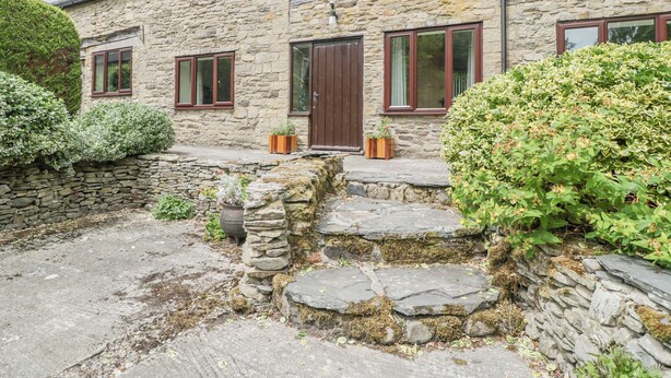A stone house with a stone staircase leading to the entrance, surrounded by greenery. - Bullfinch Cottage (Leominster)