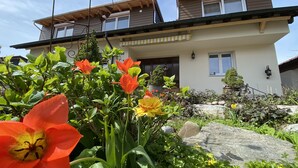 Ein zweistöckiges Haus mit einem Balkon und einem Garten voller Blumen, verbunden durch einen Kiesweg.