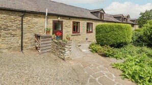 Une charmante maison en pierre avec une allée en gravier, un portail en bois et un petit jardin agrémenté de plantes en pot.