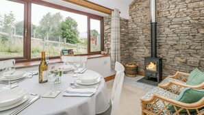 Un coin repas avec une table dressée pour quatre personnes, une cheminée en pierre et une vue sur l’extérieur.