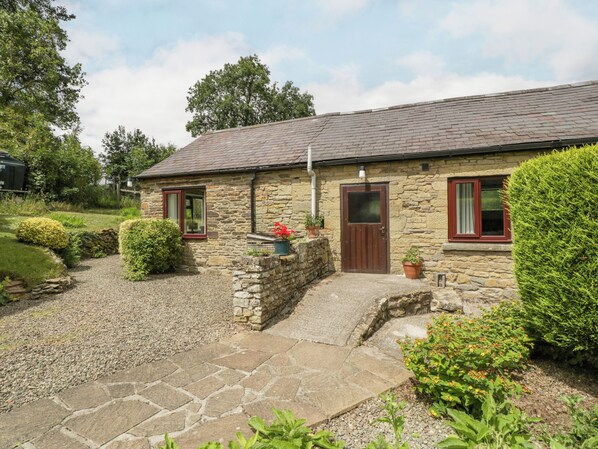 A stone cottage with a tiled roof, a gravel driveway, and a small garden with potted plants and trimmed hedges. - Fieldfare (Leominster)
