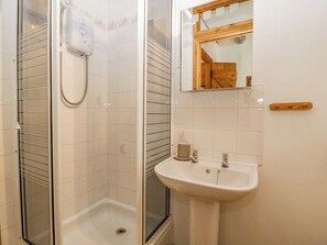 A bathroom with a glass-enclosed shower, a white sink with a wooden handle, and a mirror with a wooden frame. - Fieldfare (Leominster)