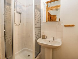 Un baño con ducha envuelta en vidrio, un lavabo blanco con pomo de madera y un espejo con marco de madera.