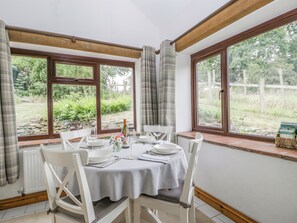 A dining area with a table set for four, large windows, and a view of the garden. - Fieldfare (Leominster)