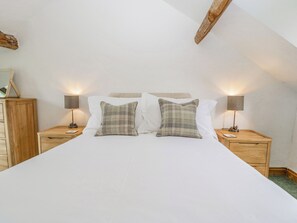 A bedroom with a large bed, two bedside tables with lamps, a wooden dresser, and a sloped ceiling. - Fieldfare (Leominster)
