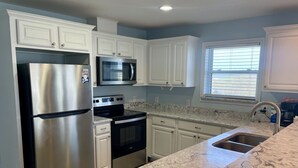 A modern kitchen with white cabinets, stainless steel appliances, and a marble countertop. - Beachgate Condo Suites And Hotel 511+512a+512b 3 Bedroom Condo (Port Aransas)