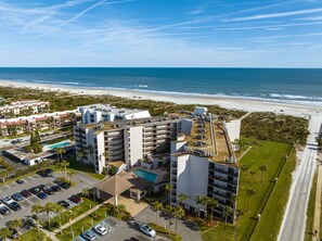 Ein Luftbild eines Hotels mit mehreren Etagen, einem Schwimmbad und Blick auf einen Strand.