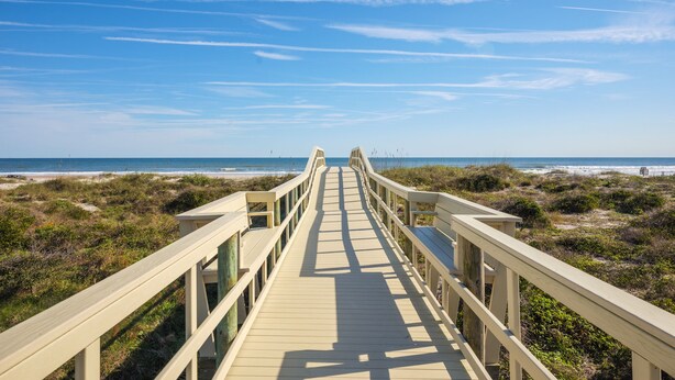 Un paseo marítimo de madera que lleva a una playa con cielo despejado.