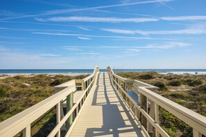 A wooden boardwalk leading to a beach with a clear sky.