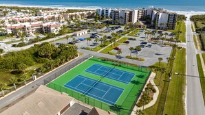 Vista aérea de una zona hotelera frente al mar, con cancha de tenis, estacionamiento y edificios.
