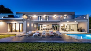 A modern two-story house with a swimming pool, outdoor seating area, and a well-lit patio. - Villa Borealis (Rasa)