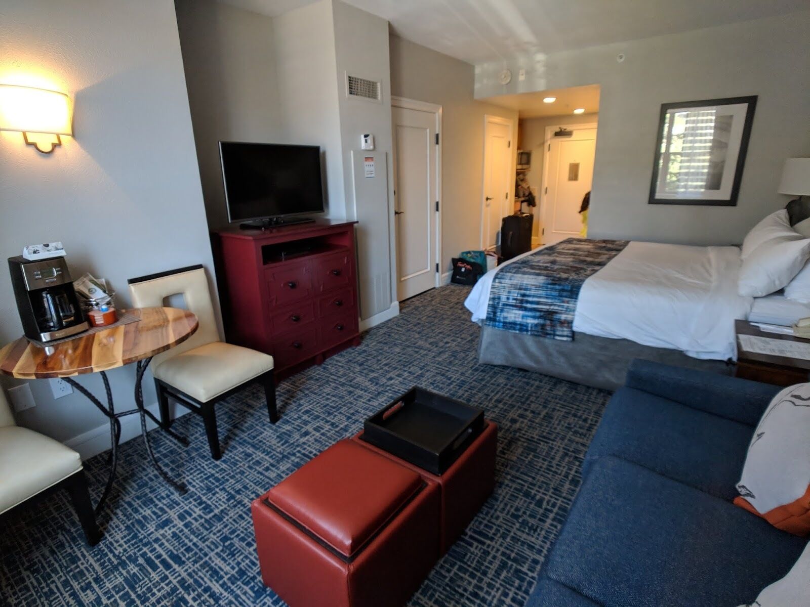 Ein Hotelzimmer mit einem Bett, einem Fernseher, einer Kaffeemaschine, einer roten Kommode, einem blauen Sofa und einem gemusterten Teppich.