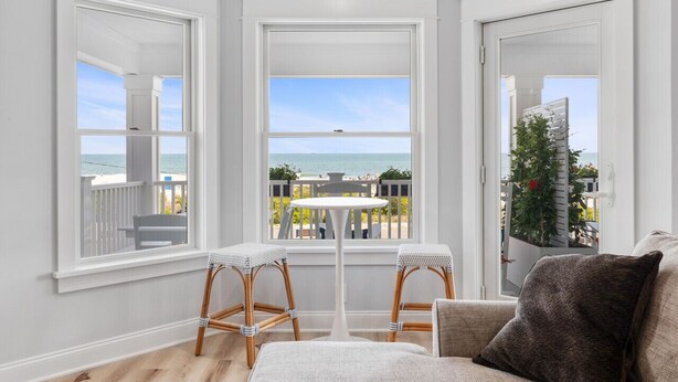 A room with large windows overlooking a balcony with a view of the sea. There are two wicker chairs and a small table in the room. - BRAND NEW OCEANFRONT 3 Bedroom 2 bath 1st floor villa (Honu) (Cape May)