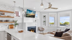 A modern kitchen with white cabinetry, a fireplace, and a large island. There are shelves with dishes and a hanging light fixture. - BRAND NEW OCEANFRONT 3 Bedroom 2 bath 1st floor villa (Honu) (Cape May)